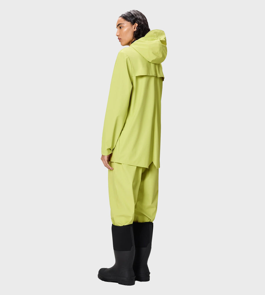 Person wearing a bright green raincoat and pants with black boots on a white background