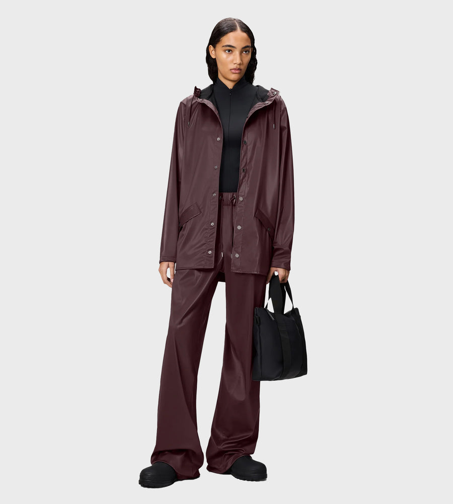 Person wearing a maroon raincoat and pants with a black bag on a light gray background