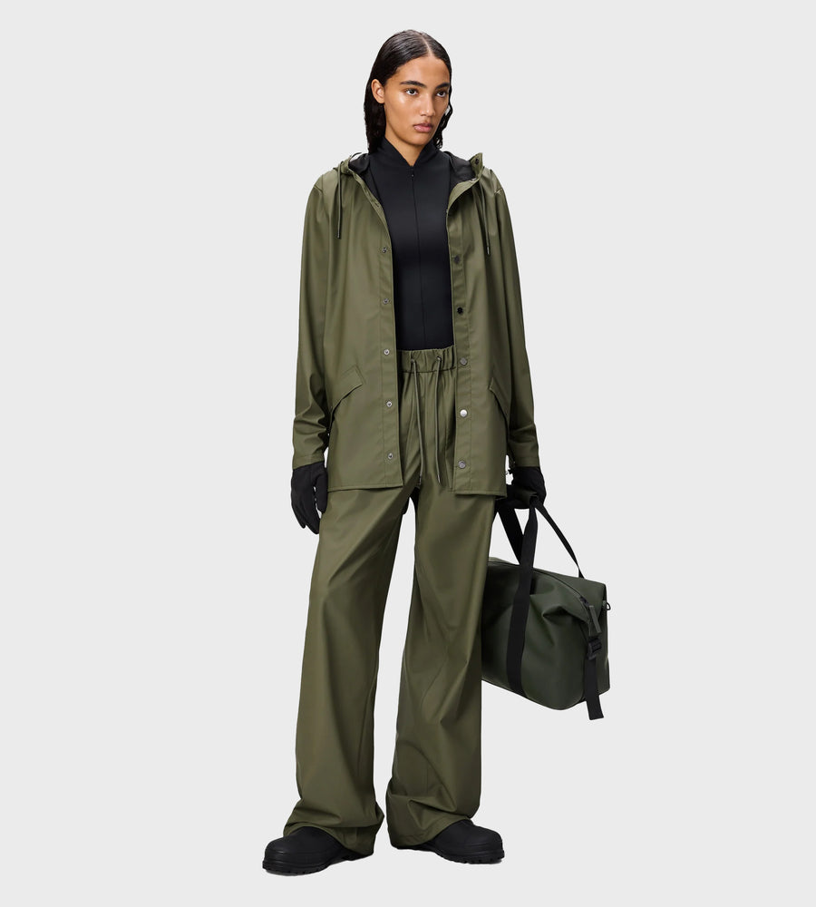 Person wearing a green raincoat and pants holding a bag on a white background