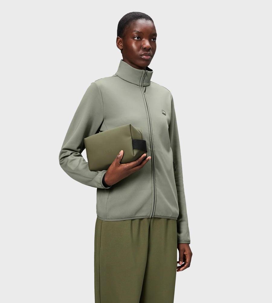 Person wearing a green jacket holding a green clutch against a white background