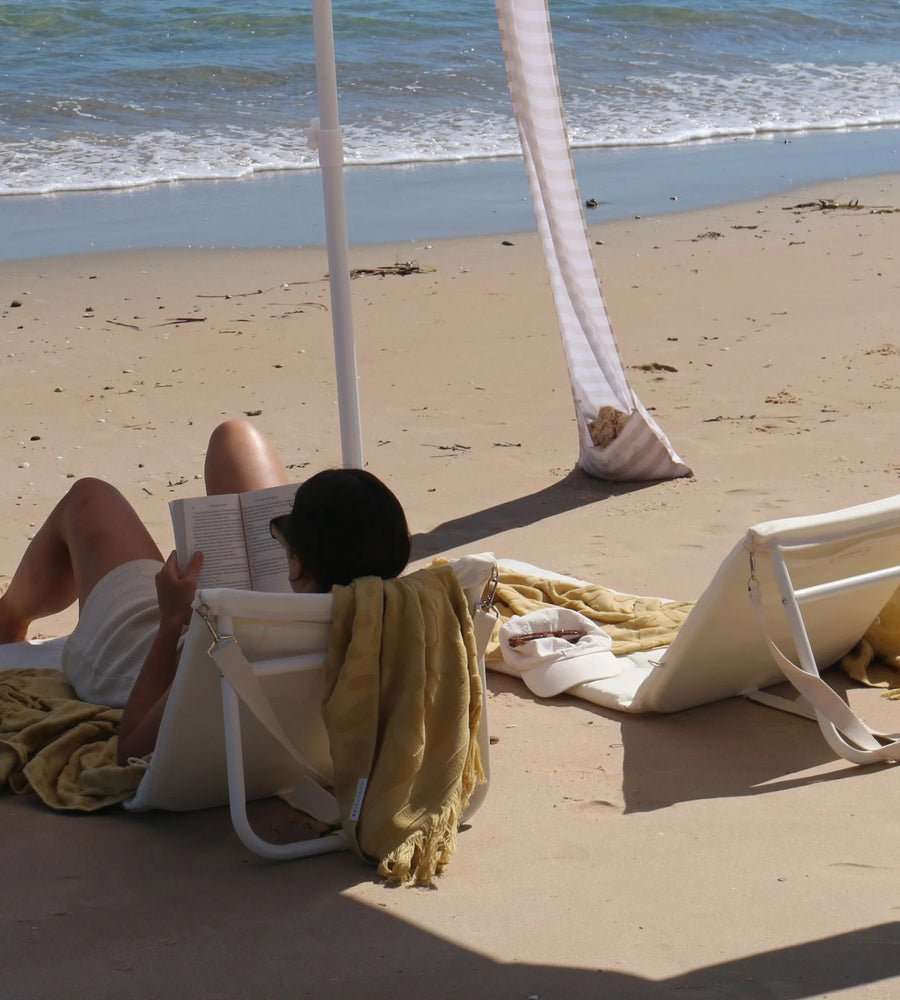Person reading a book on a beach chair by the ocean