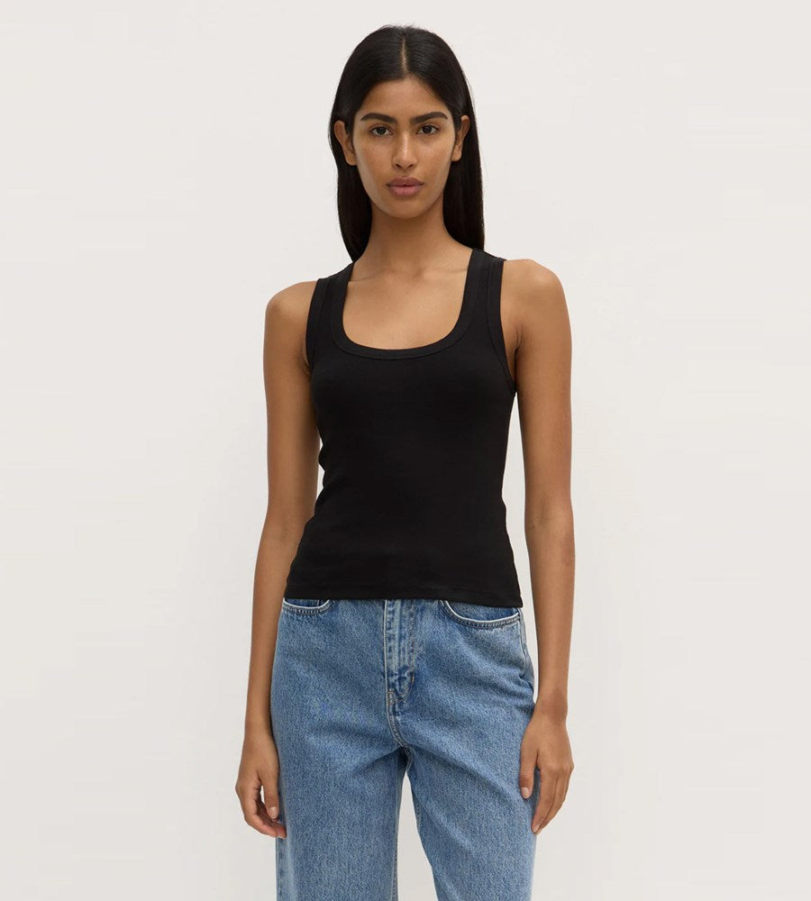 Woman wearing a black tank top and blue jeans against a plain background