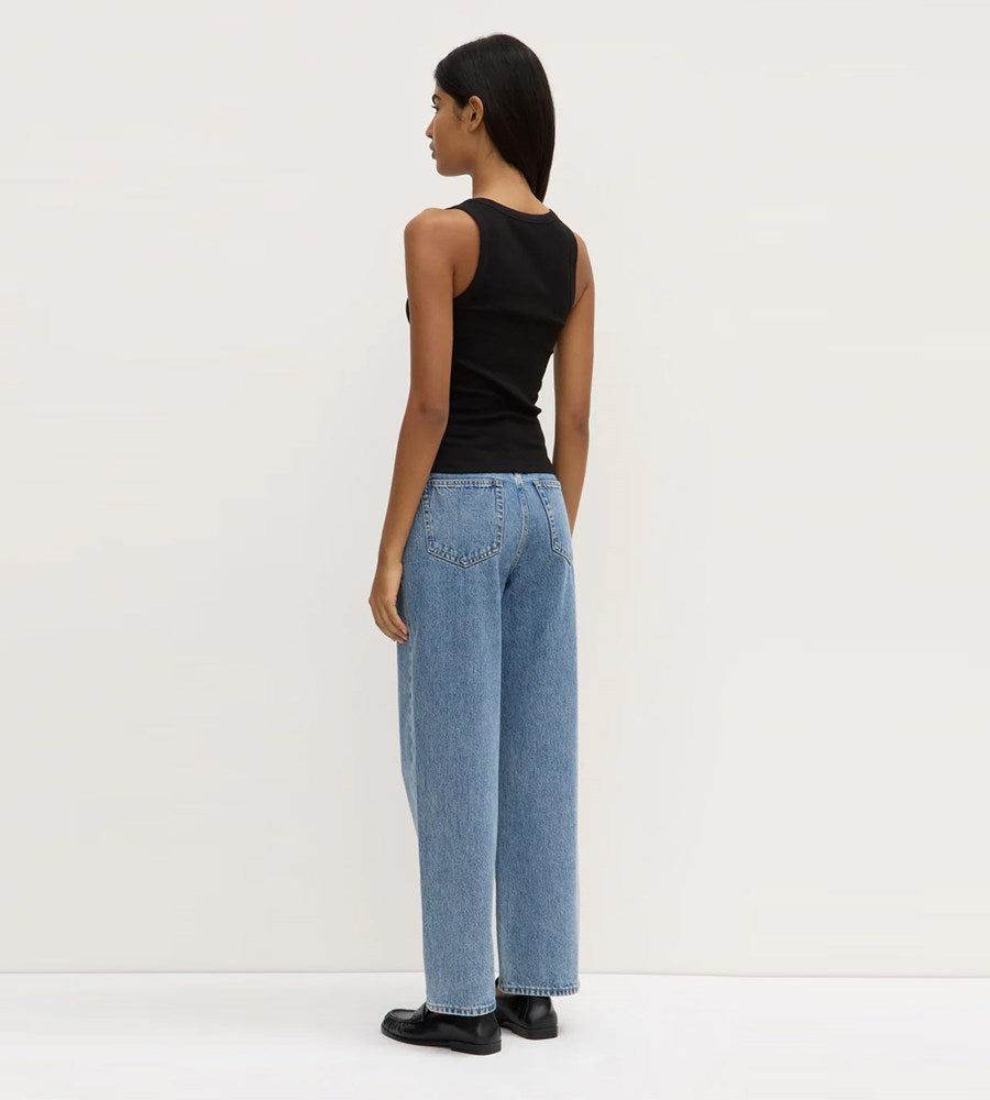 Person wearing a black sleeveless top and light blue jeans on a white background
