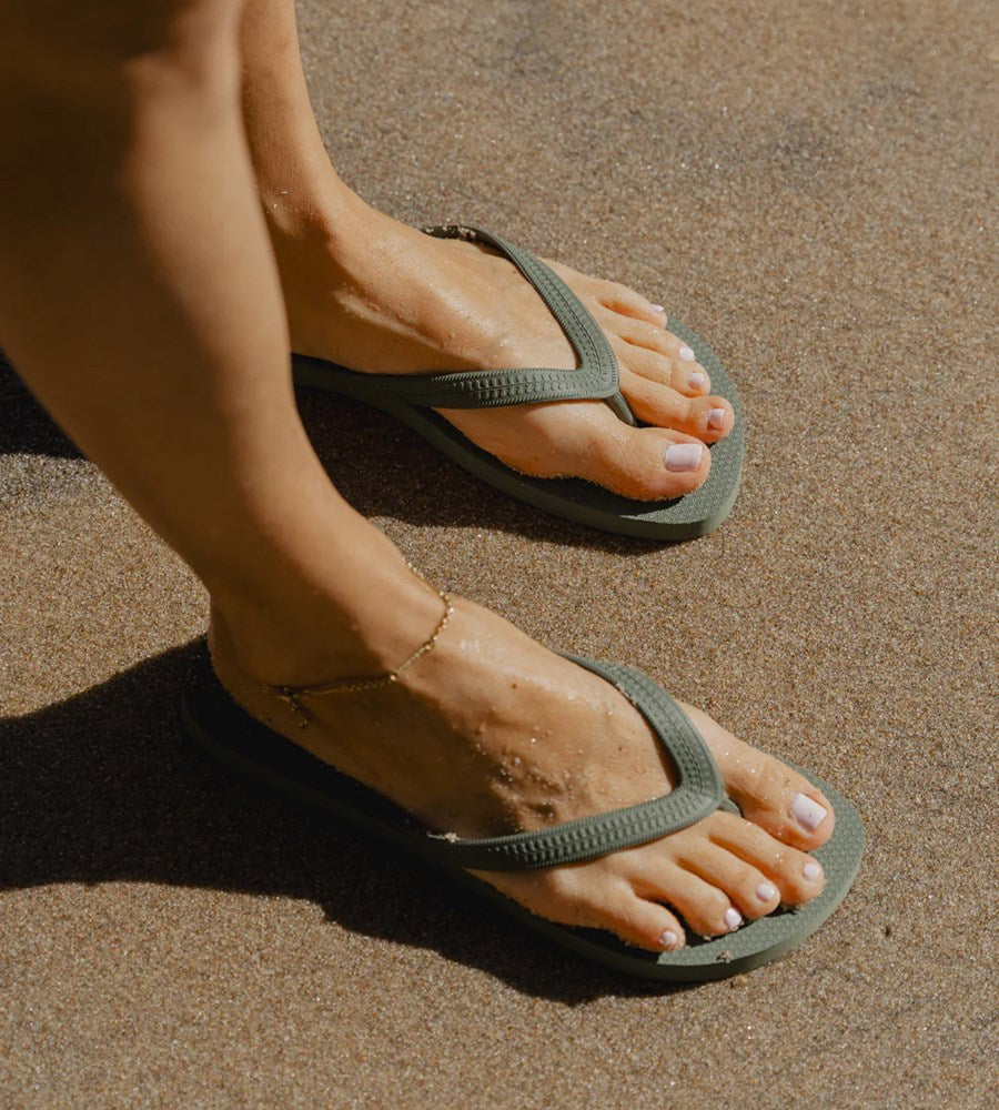 Person wearing green flip-flops on a sandy surface