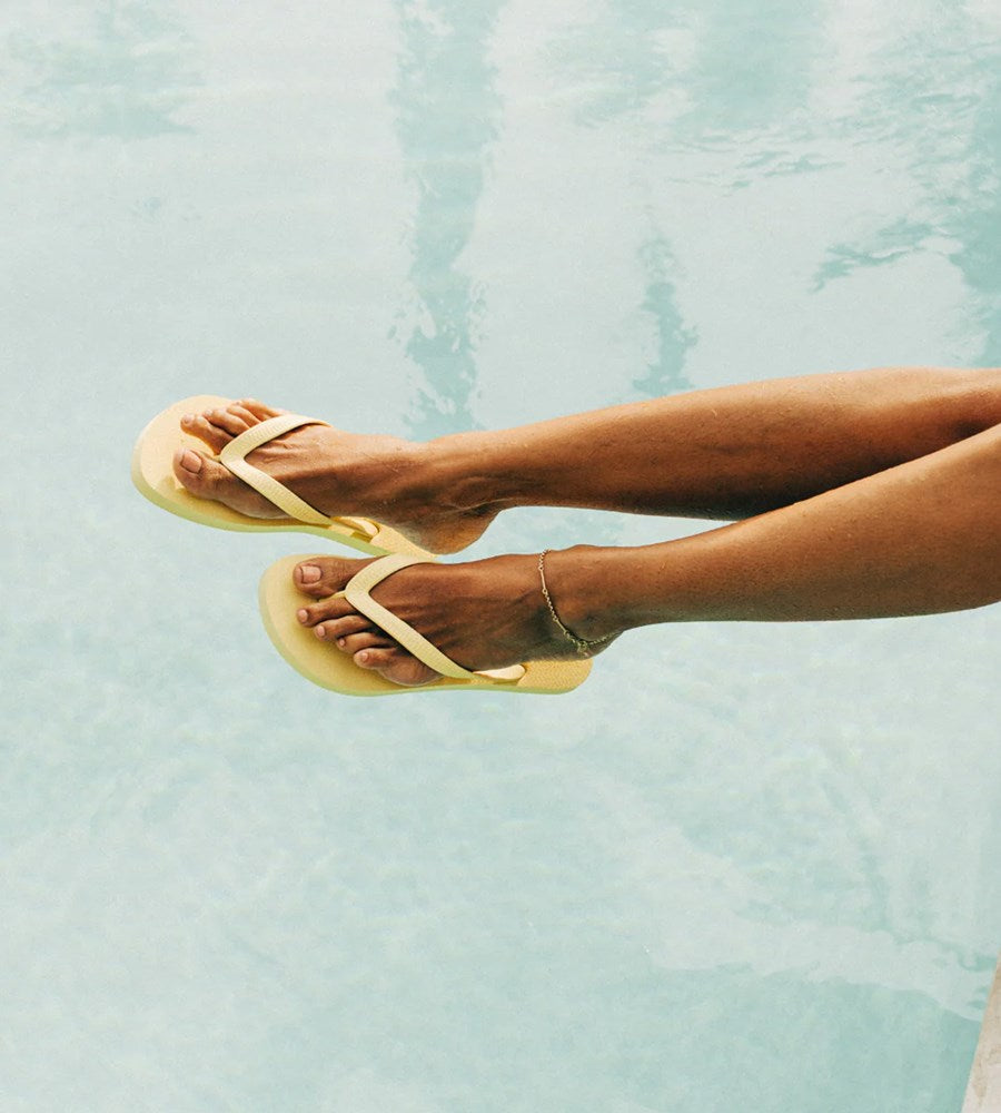 Person wearing yellow sandals with a light blue water background