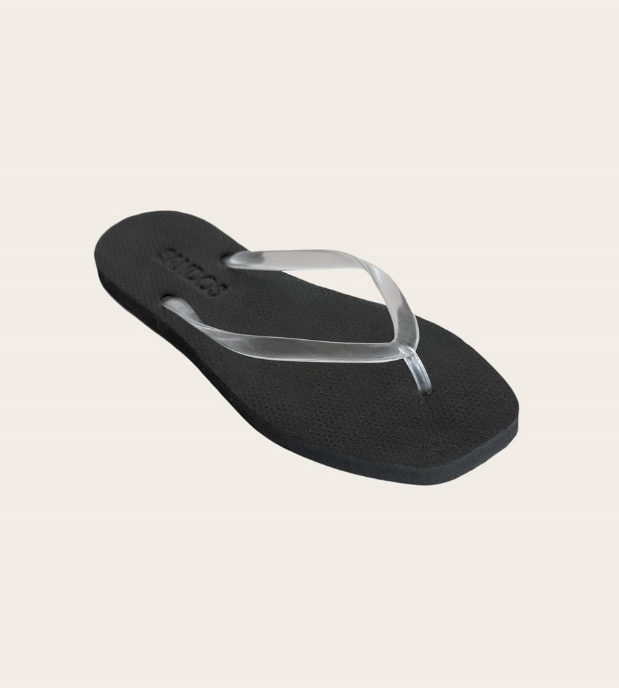 Black flip-flop sandal with a white strap on a beige background