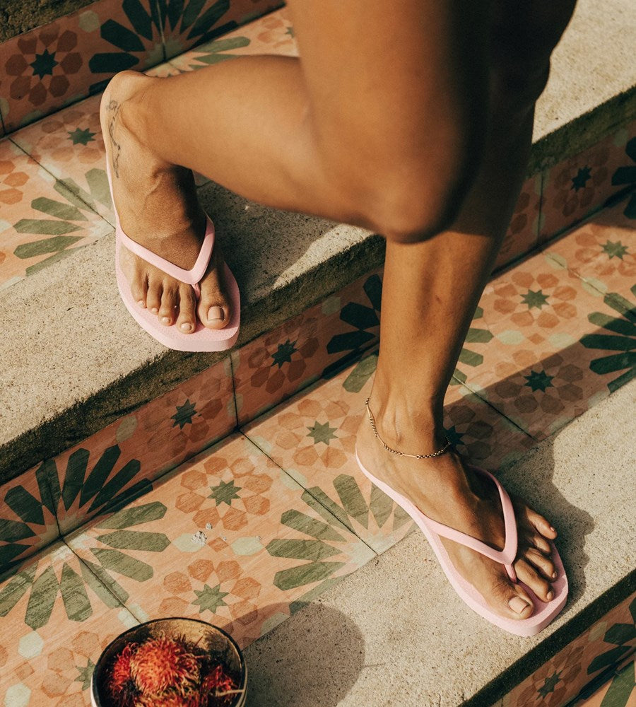 Person wearing pink flip-flops on a patterned tile floor