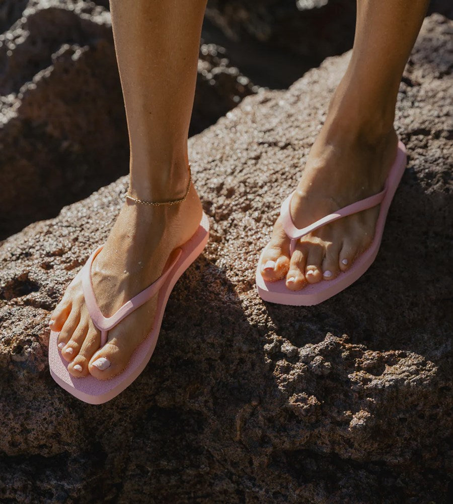 Person wearing pink flip-flops on a rocky surface