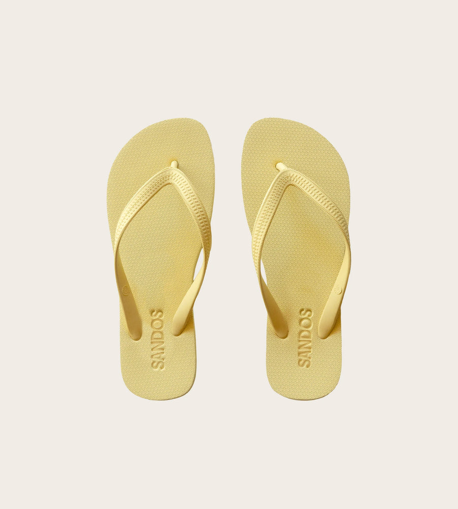 Pair of yellow flip-flops with 'SANDOS' branding on a light beige background