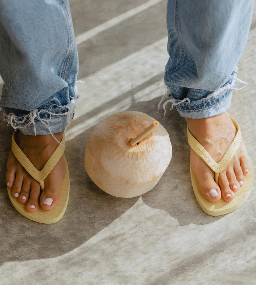 Person wearing yellow sandals next to a coconut on a concrete surface