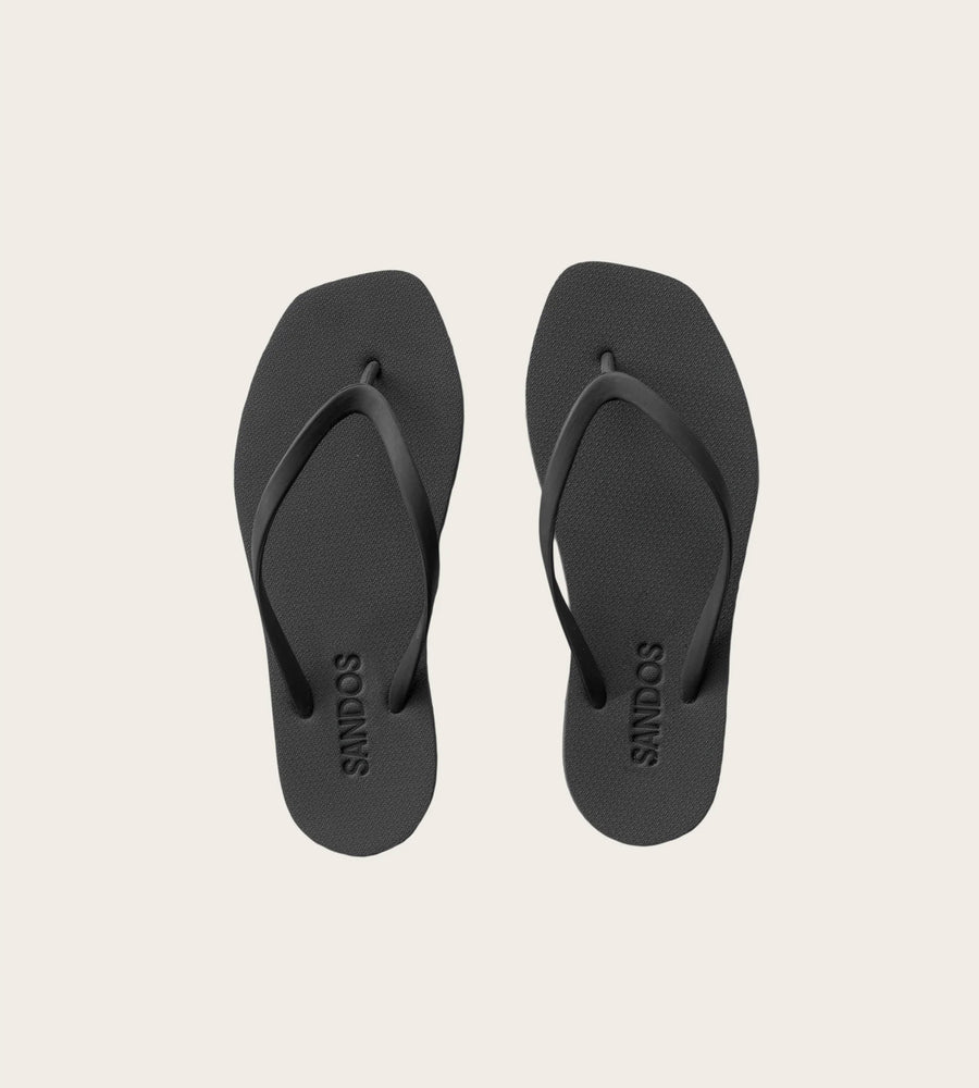 Pair of black sandals with sandos branding on a beige background