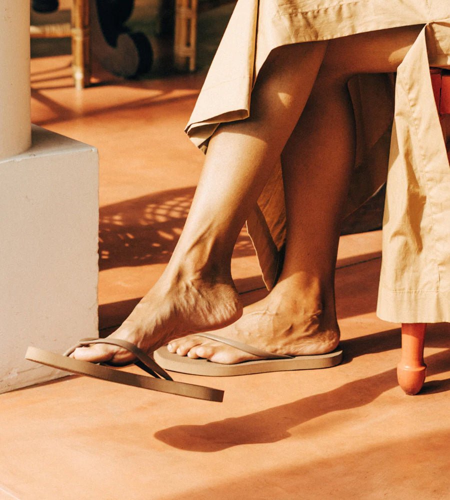 Person wearing sandals on a wooden floor with a beige skirt.