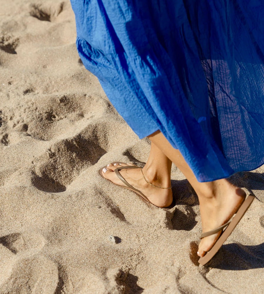 Person wearing a blue dress and sandals on a sandy beach