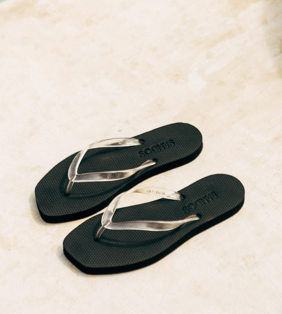 Black flip-flops with silver straps on a textured beige surface