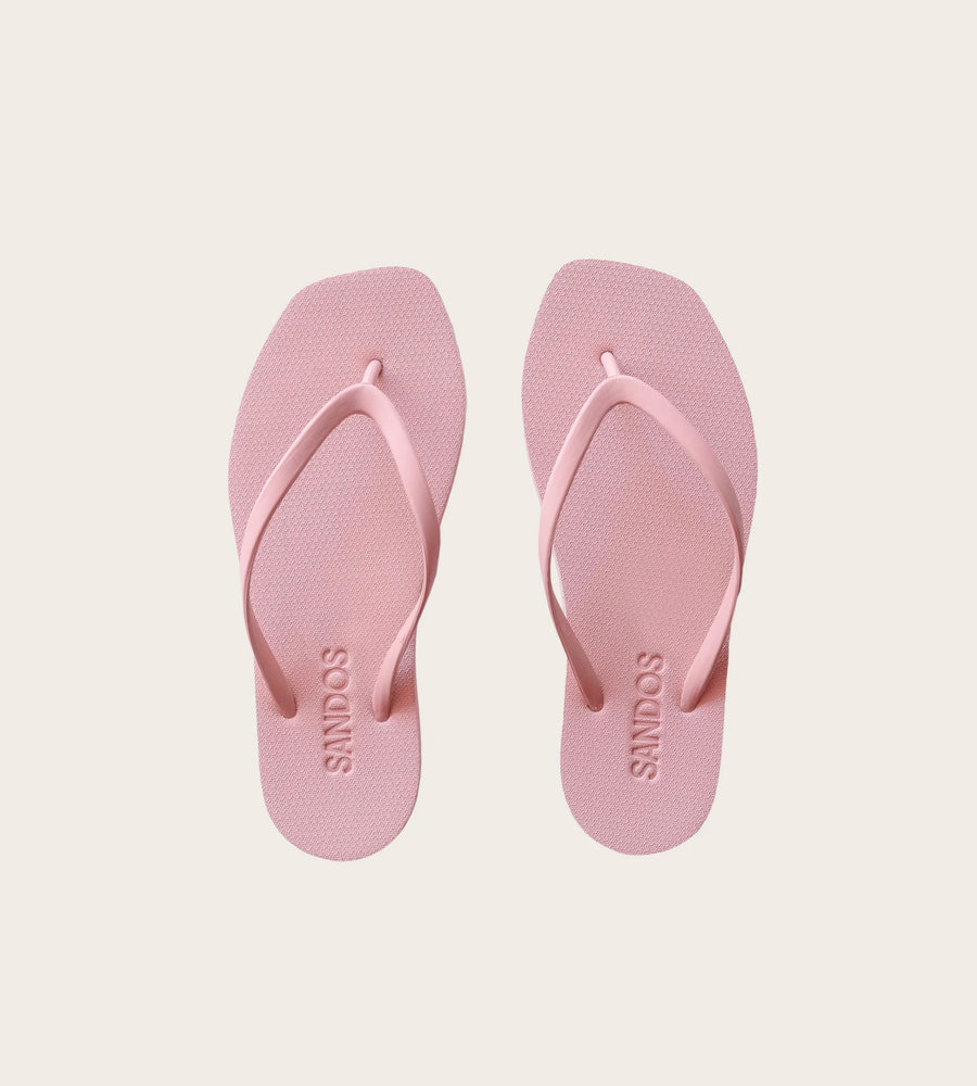 Pair of pink flip-flops with 'SANDOS' branding on a light beige background