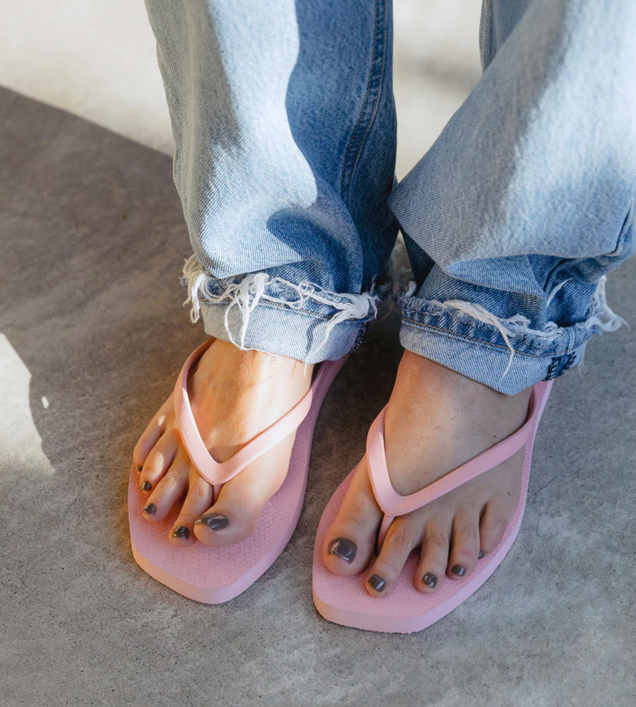 Person wearing pink flip-flops with rolled-up jeans on a neutral background