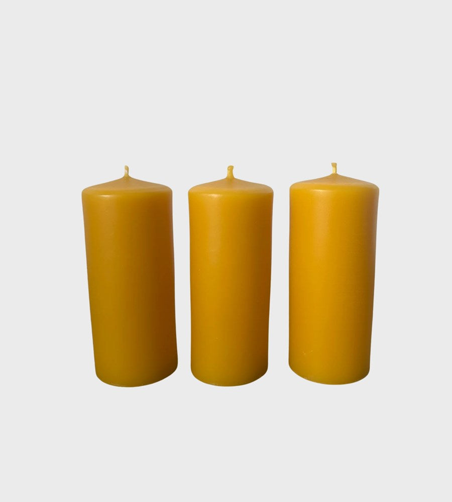 Three yellow candles of different sizes on a light gray background