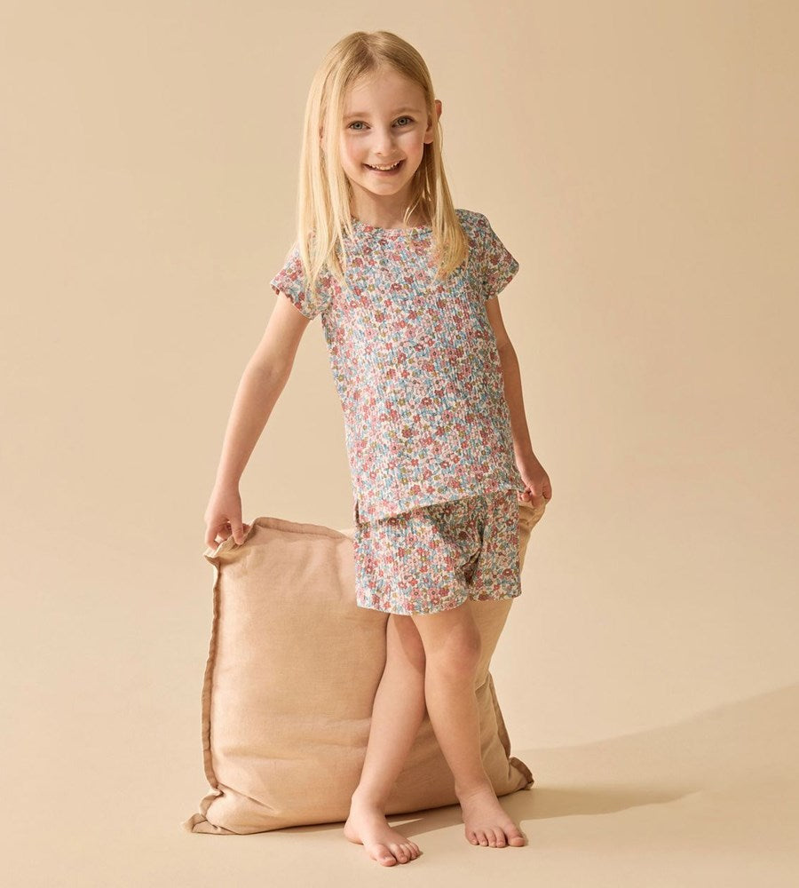 Young girl in a floral outfit standing next to a beige bag on a beige background