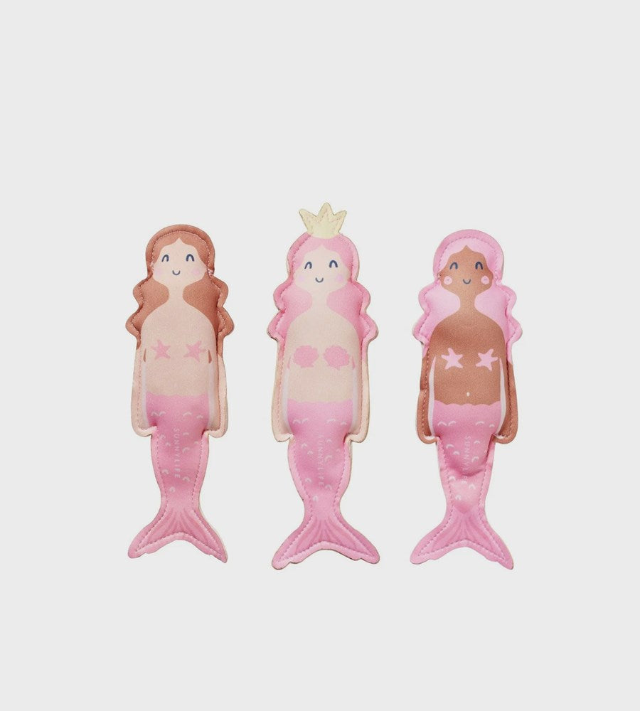 Three mermaid figurines with different skin tones on a light pink background