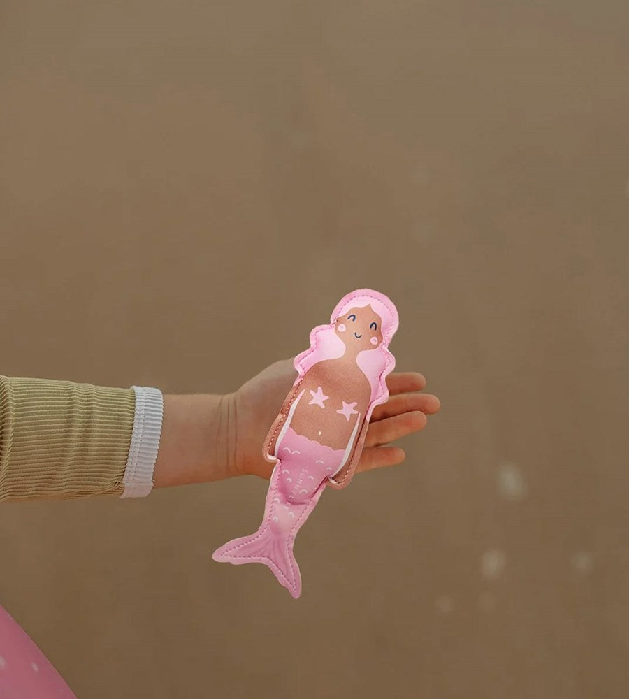 Hand holding a pink mermaid toy against a brown background