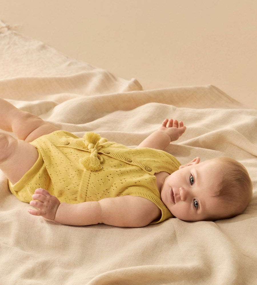 Baby wearing a yellow outfit lying on a soft beige blanket