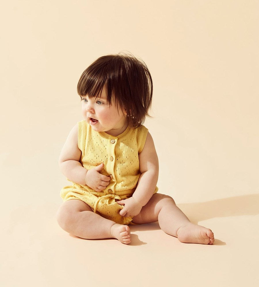 Baby in a yellow outfit sitting on a beige background