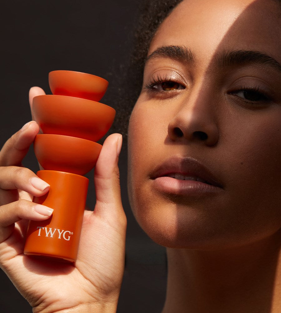 Person holding a 'TWYG'  product branding close to their face against a dark background