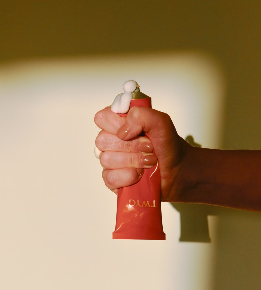 Hand holding a red lip balm with visible brand name against a neutral background