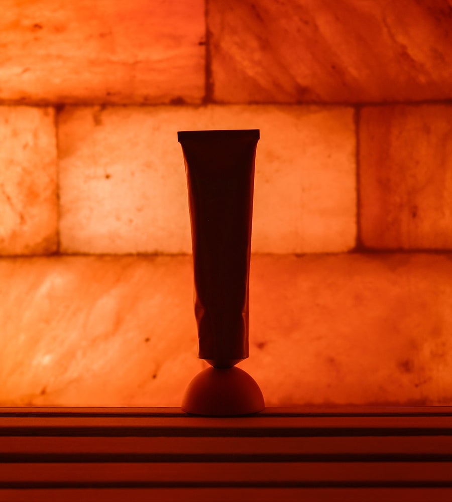 Black tube of cream on a reflective surface with a warm, orange-toned background