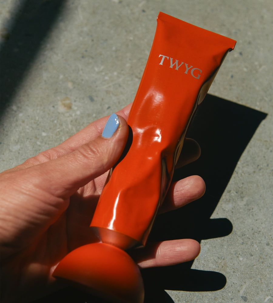 Orange hair product packet with 'TWYG' branding held by a hand on a concrete surface.