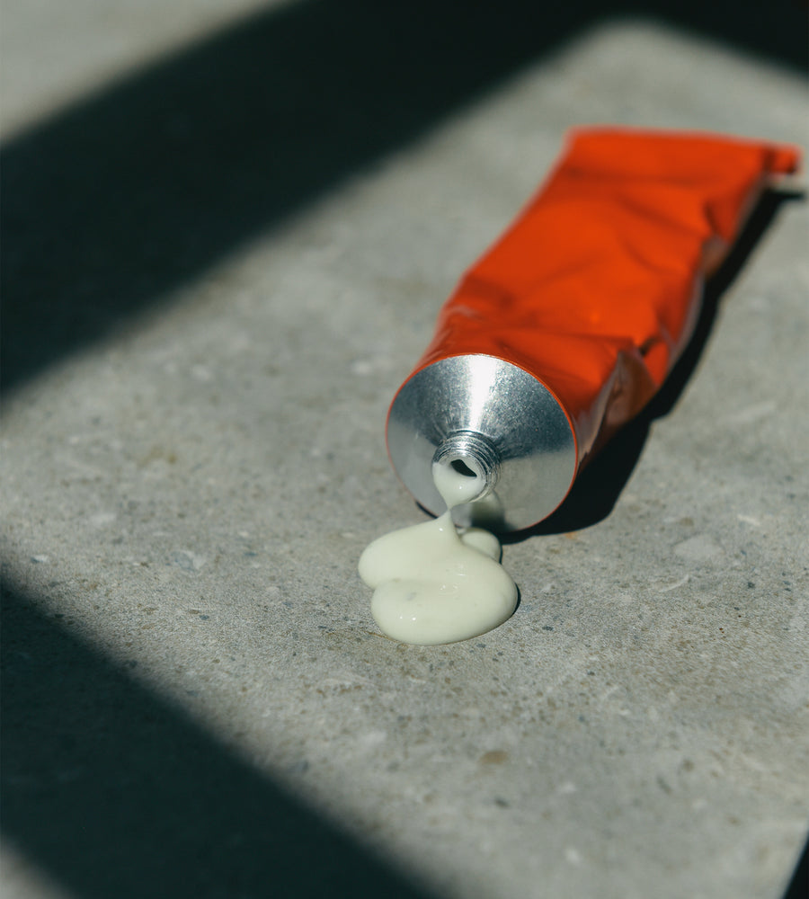 Red tube of cream with white cream oozing out on a concrete surface