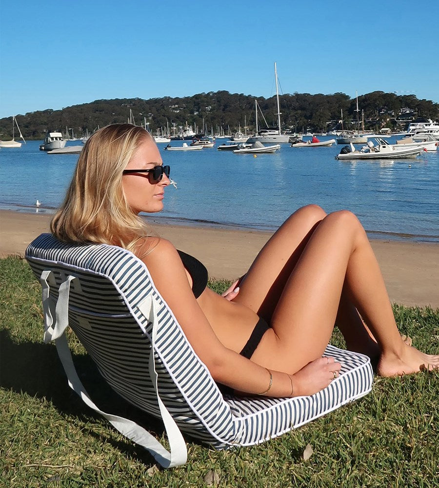 Woman sitting on a striped chair by the beach with boats in the background