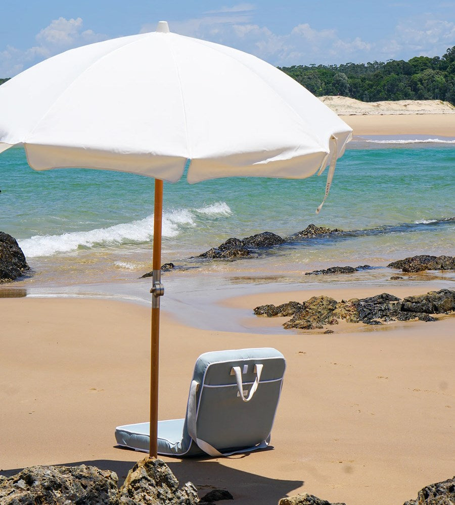 Beach chair with a white umbrella on a sandy beach with ocean and sky in the background