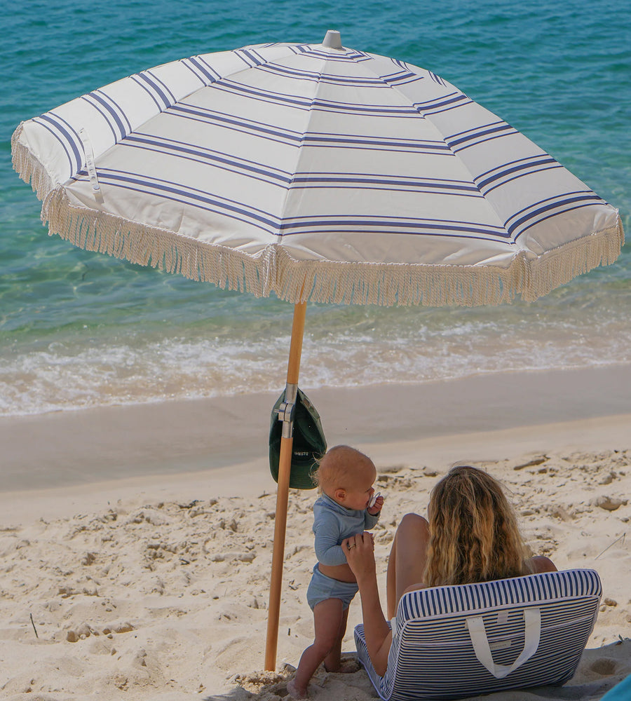 Woman and child under a striped beach umbrella on a sandy beach with ocean in the background