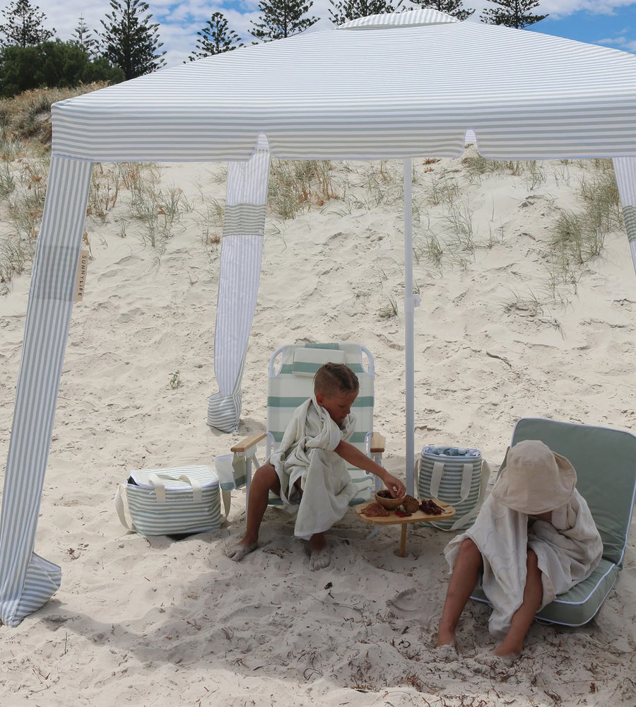 Two children playing on a sandy beach under a striped canopy.