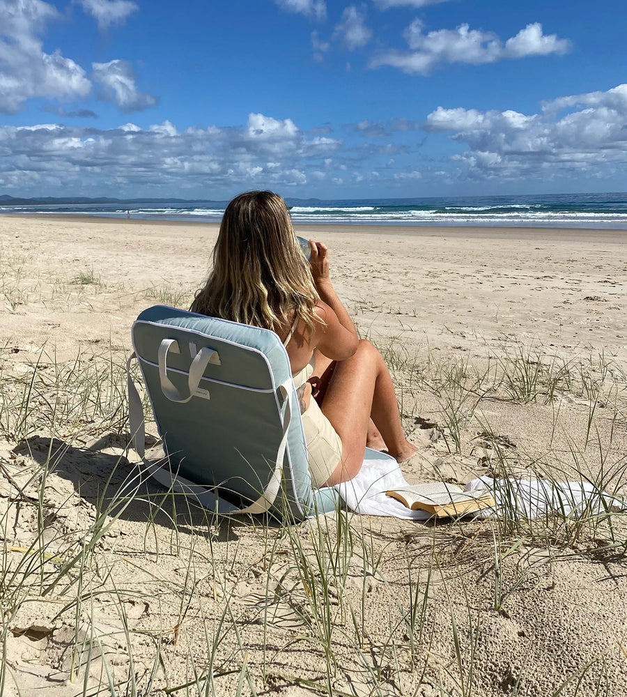 Person sitting on a beach chair reading a book with a scenic ocean view.