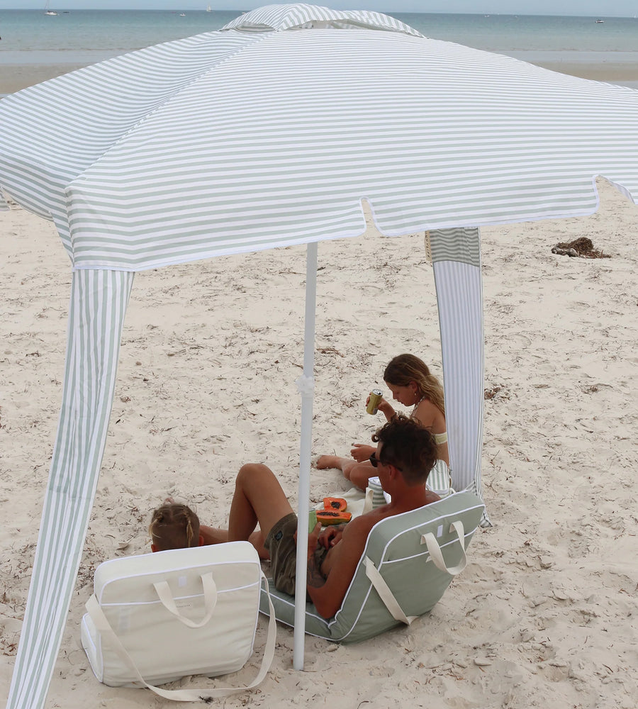 People relaxing under a striped beach canopy on a sandy beach.