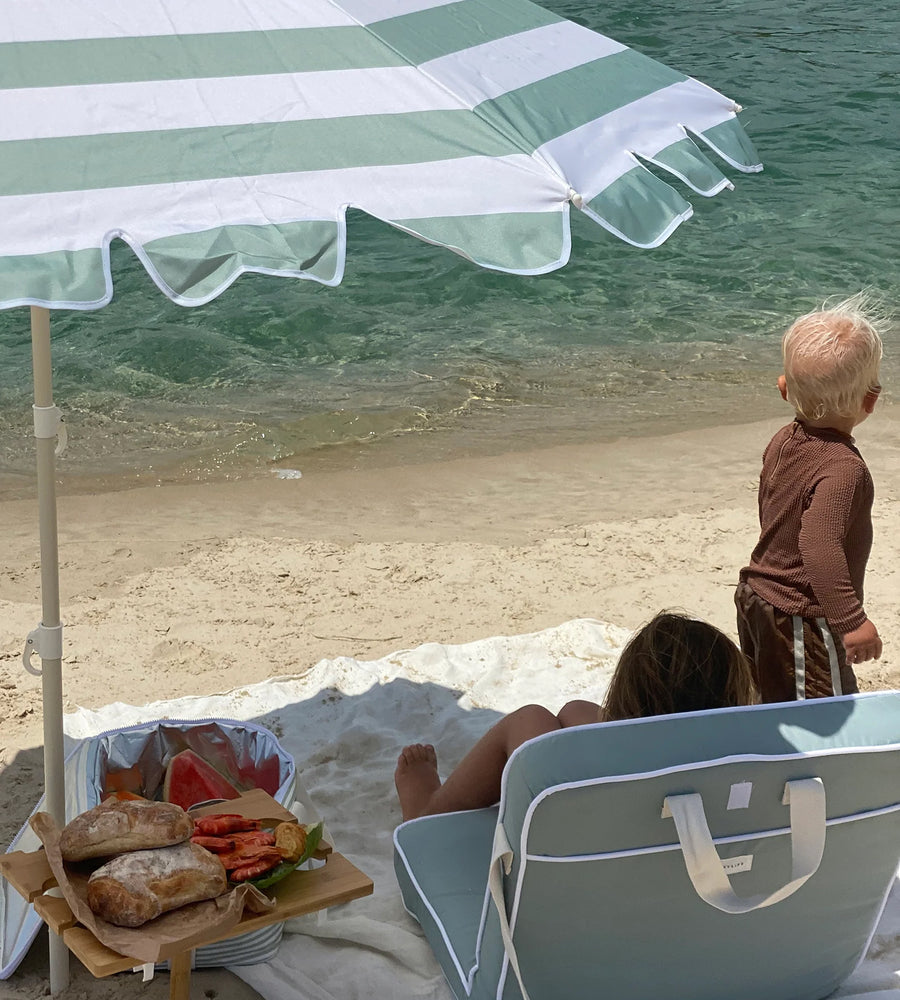 Beach scene with a child, beach chair, and striped umbrella.