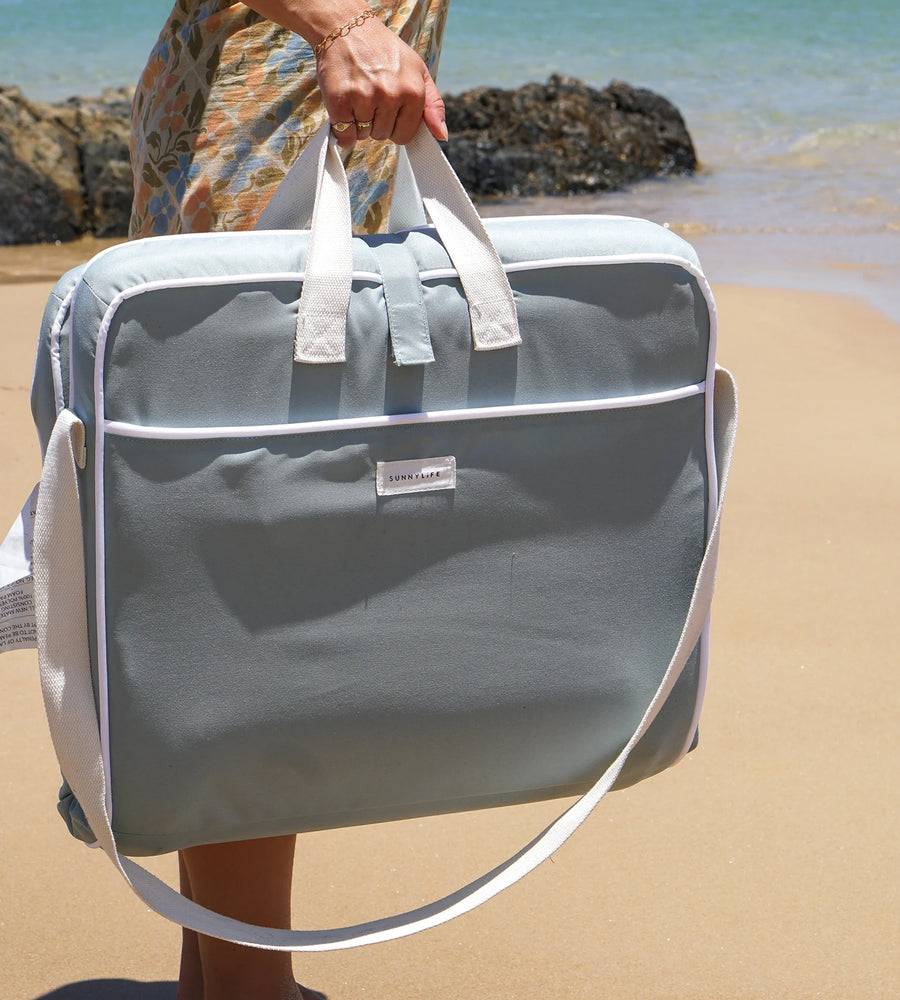 Person holding a gray duffel bag with a beach in the background