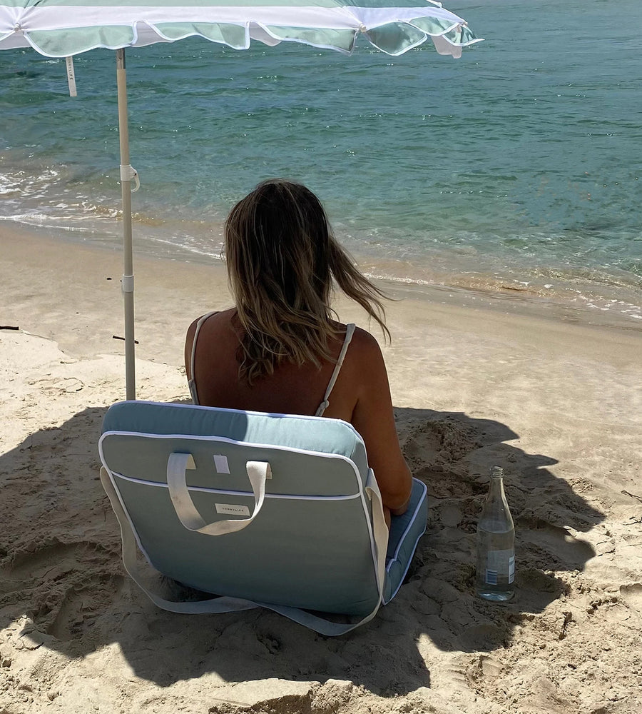 Woman sitting on a beach chair under an umbrella with ocean view