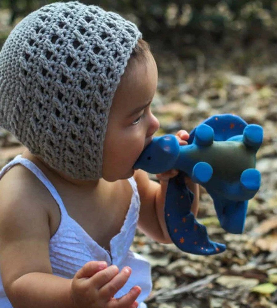 Baby wearing a textured gray hat holding a blue teething toy outdoors.
