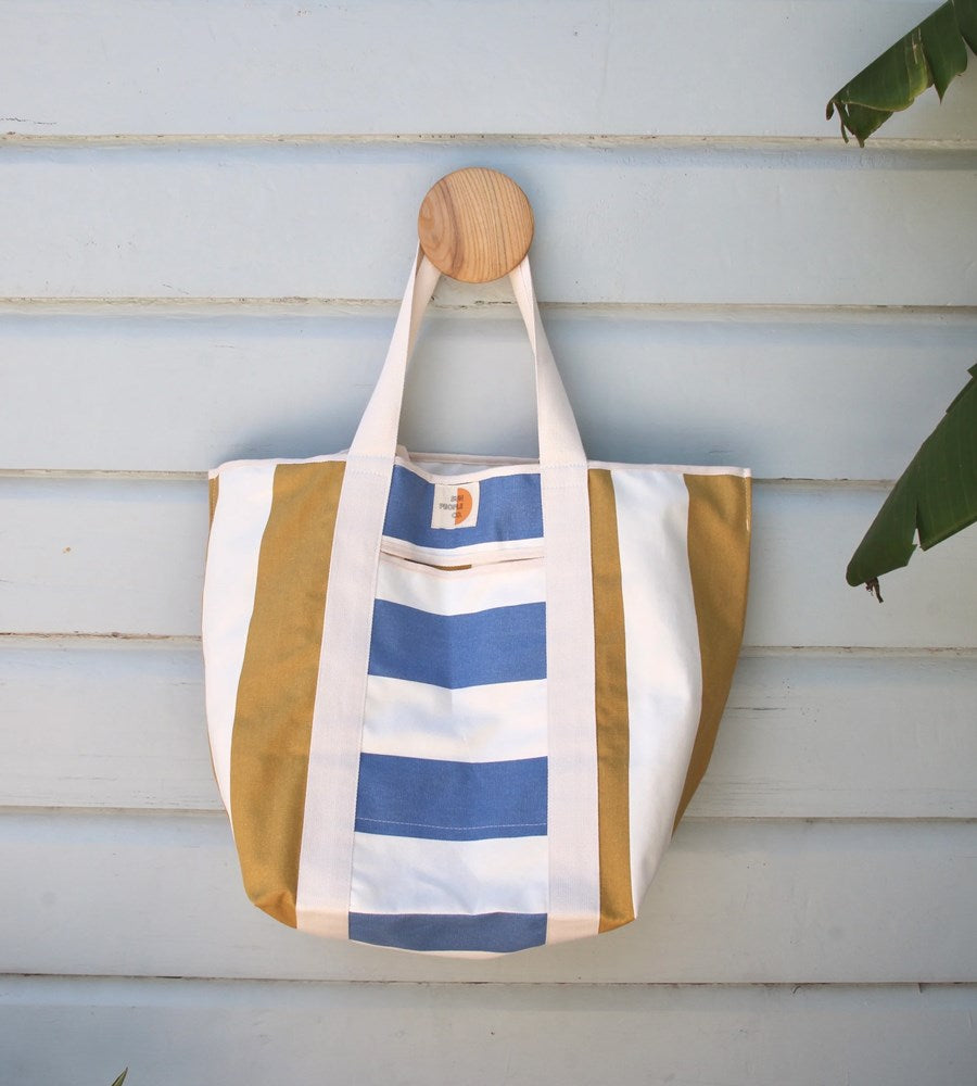 Striped tote bag with blue and beige stripes hanging on a wooden surface.