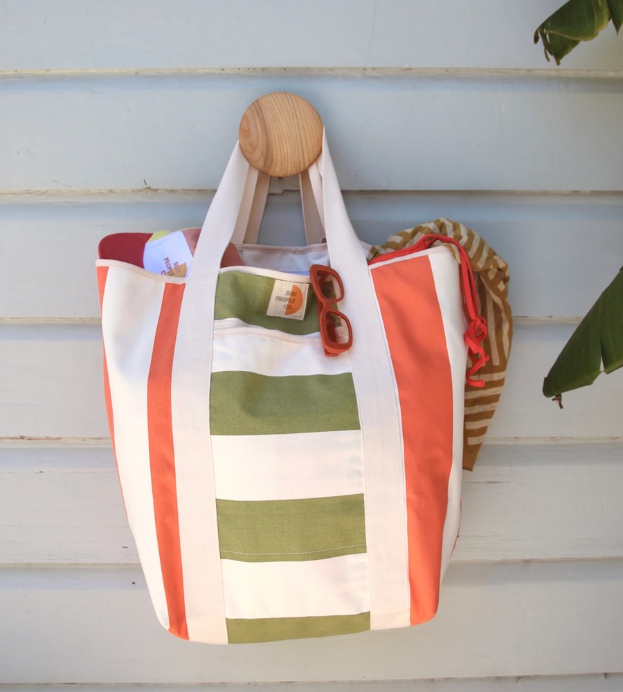 Striped beach bag with wooden handle hanging on a wooden surface
