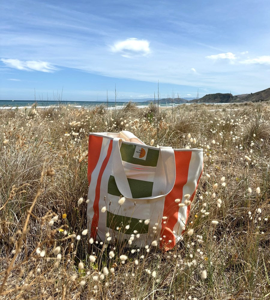 Straw bag with green and orange design on a beach with grass and ocean in the background