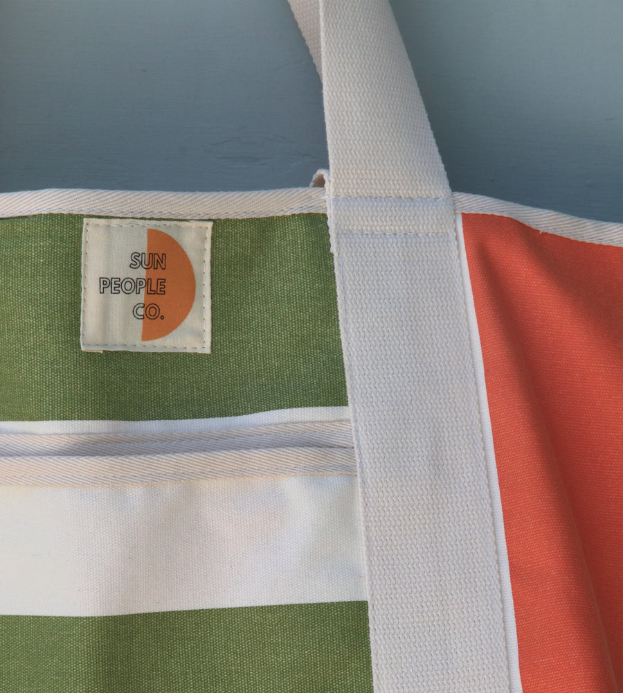 Tote bag with green, white, and orange stripes and a visible brand label on a light blue background.