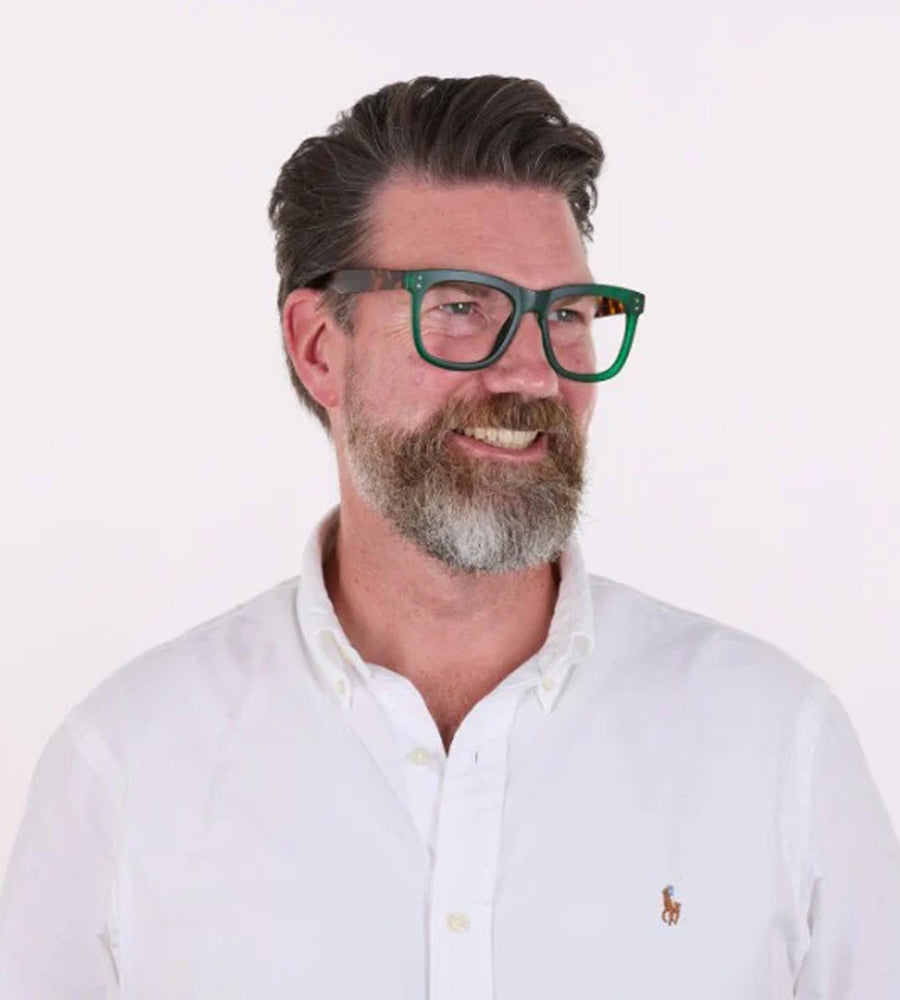 Man wearing green glasses and a white shirt with a logo on a white background