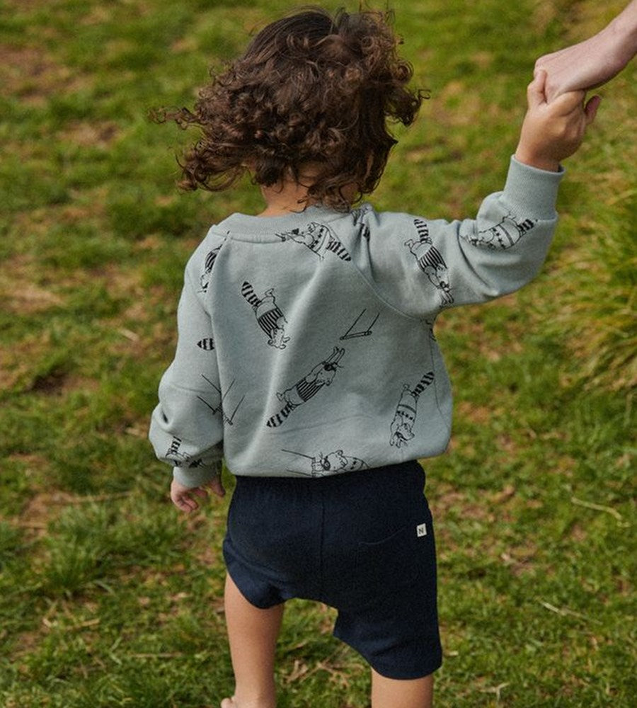 Child wearing a light blue hoodie with black patterns, standing on grass.