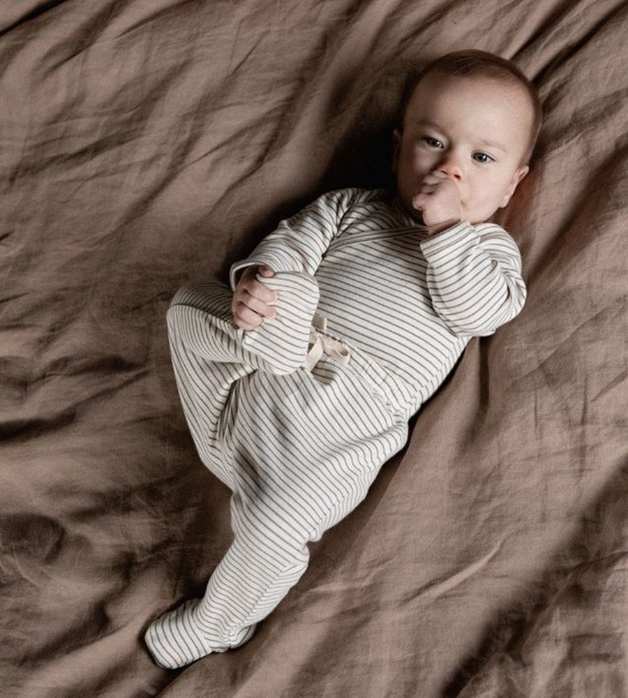 Baby in a striped onesie lying on a brown blanket