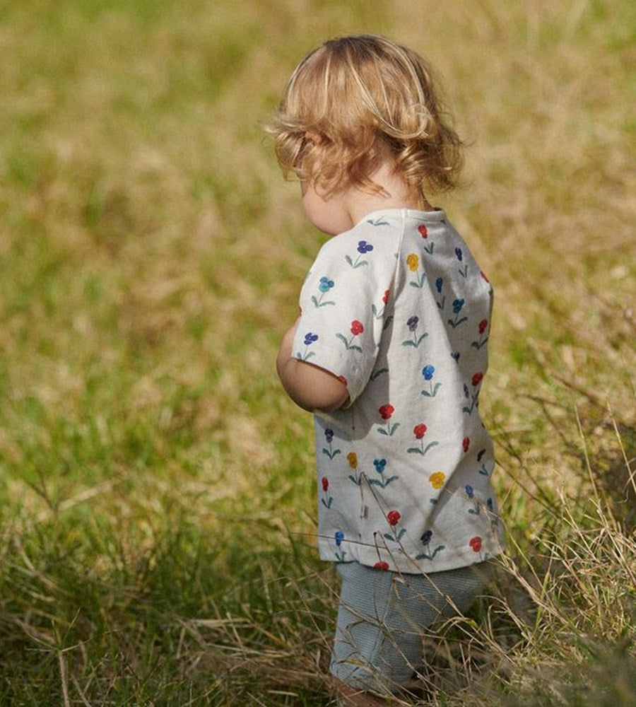 Child wearing a shirt with floral patterns standing in a grassy field