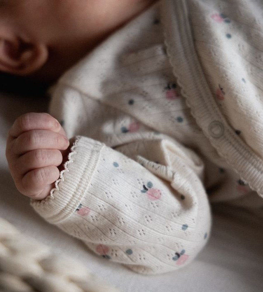 Close-up of a baby's hand wearing a white textured bootie with floral patterns.